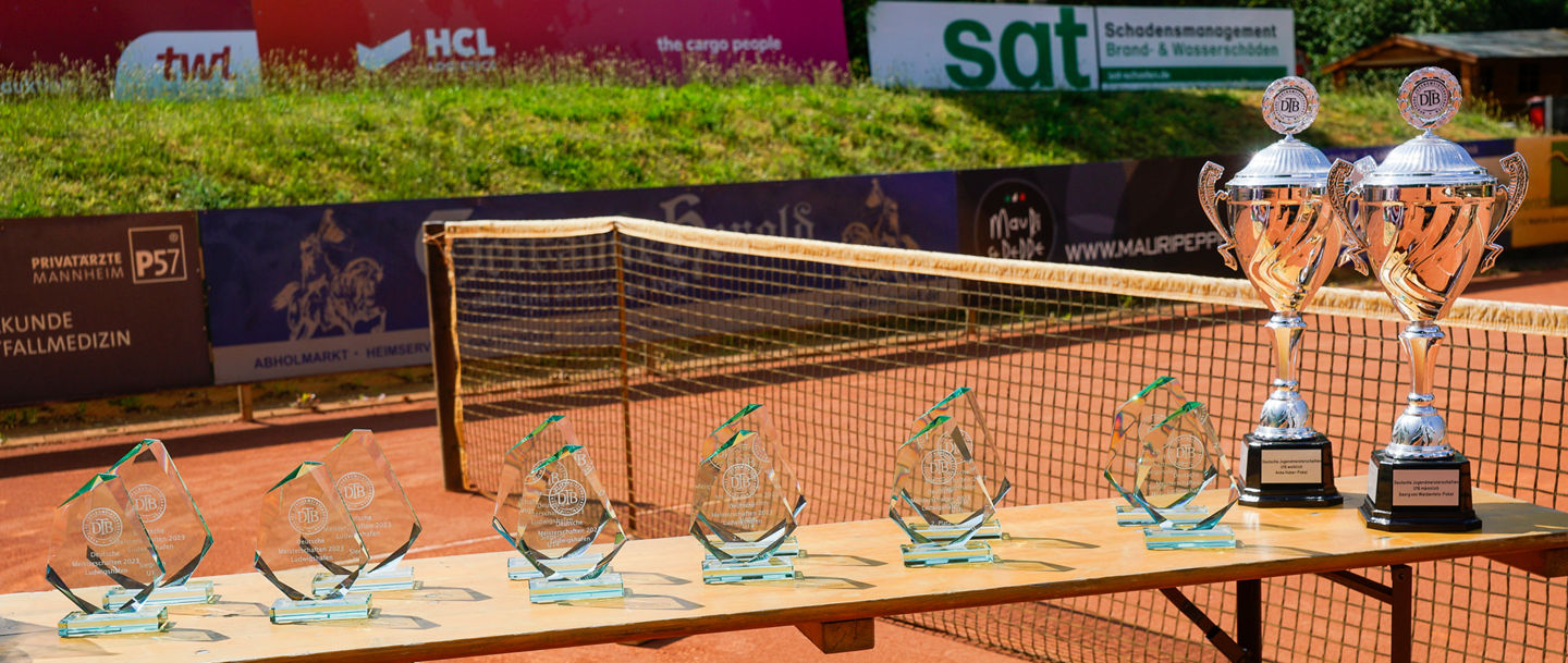 Pokale der Deutschen Jugend-Meisterschaften auf einem Tisch, der vor einem Tennisnetz steht
