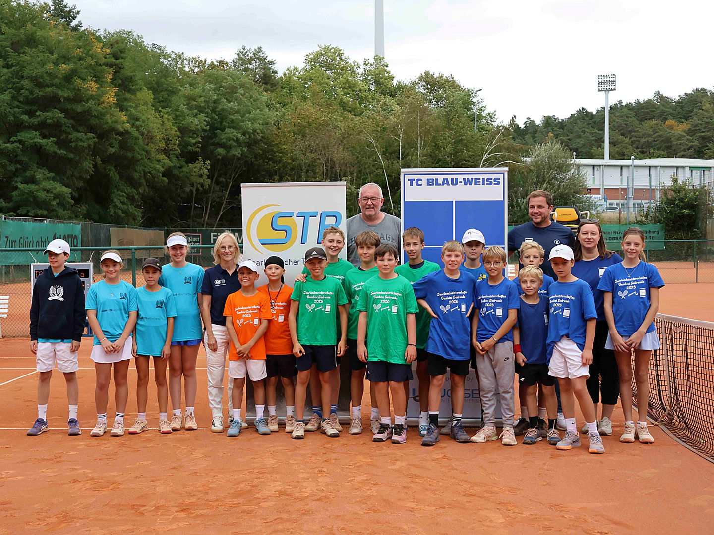 Alle 4 teilnehmenden Mannschaften in unterschiedlich farbigen, einheitlichen Shirts auf dem Tennisplatz zum Gruppenfoto aufgestellt