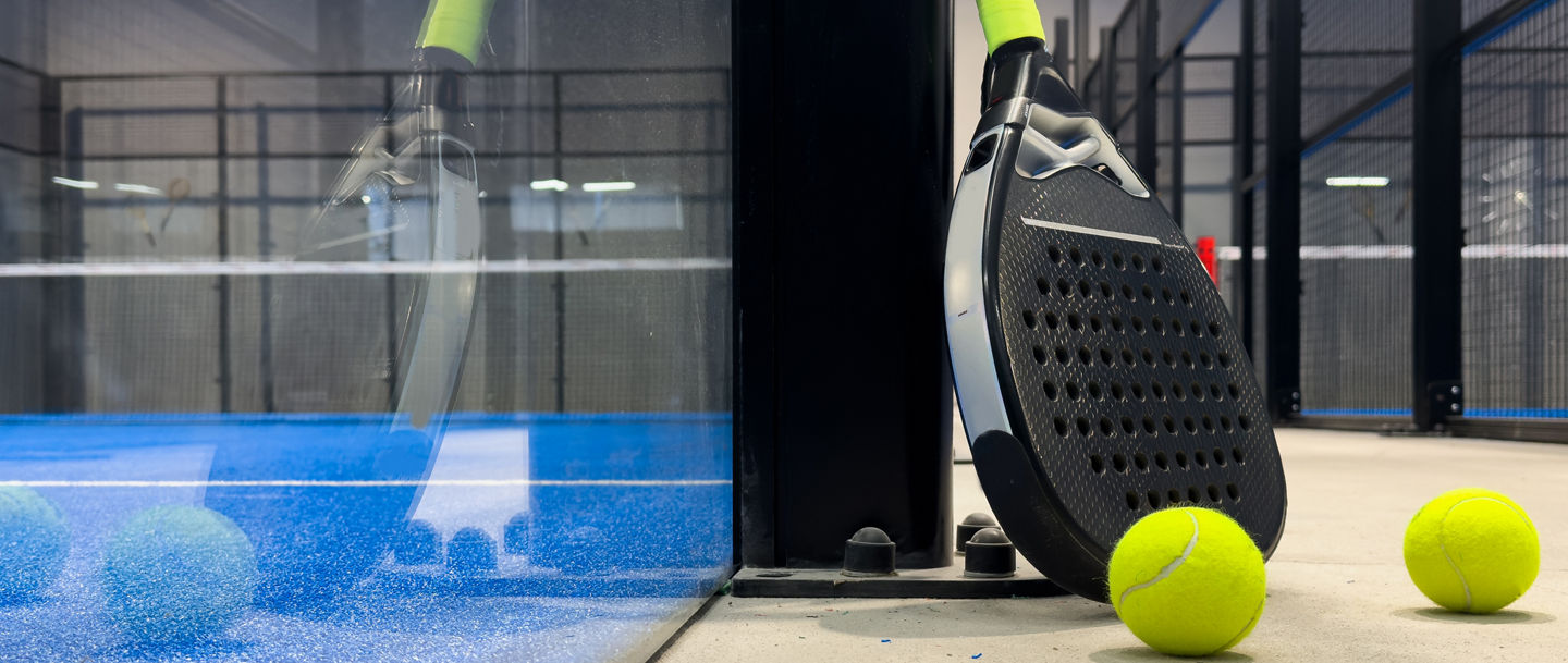 Padelschläger mit Bällen vor einem Court 