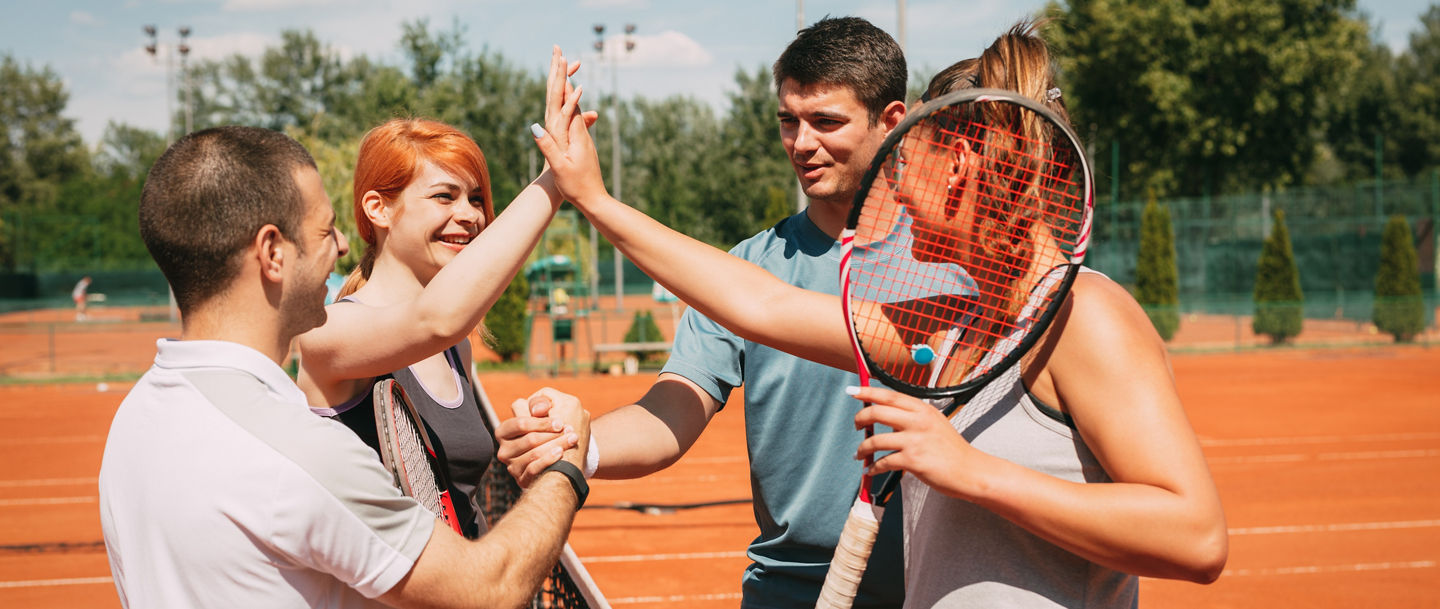 Four young friends giving a high-five after tennis training. Selective focus.