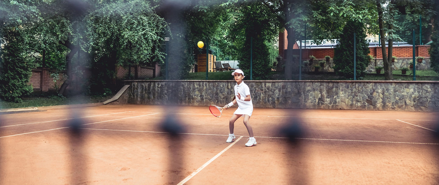 Full length shot of a sporty little girl on open tennis court. Child girl athlete playing tennis in the sport club. Active exercise for kids.