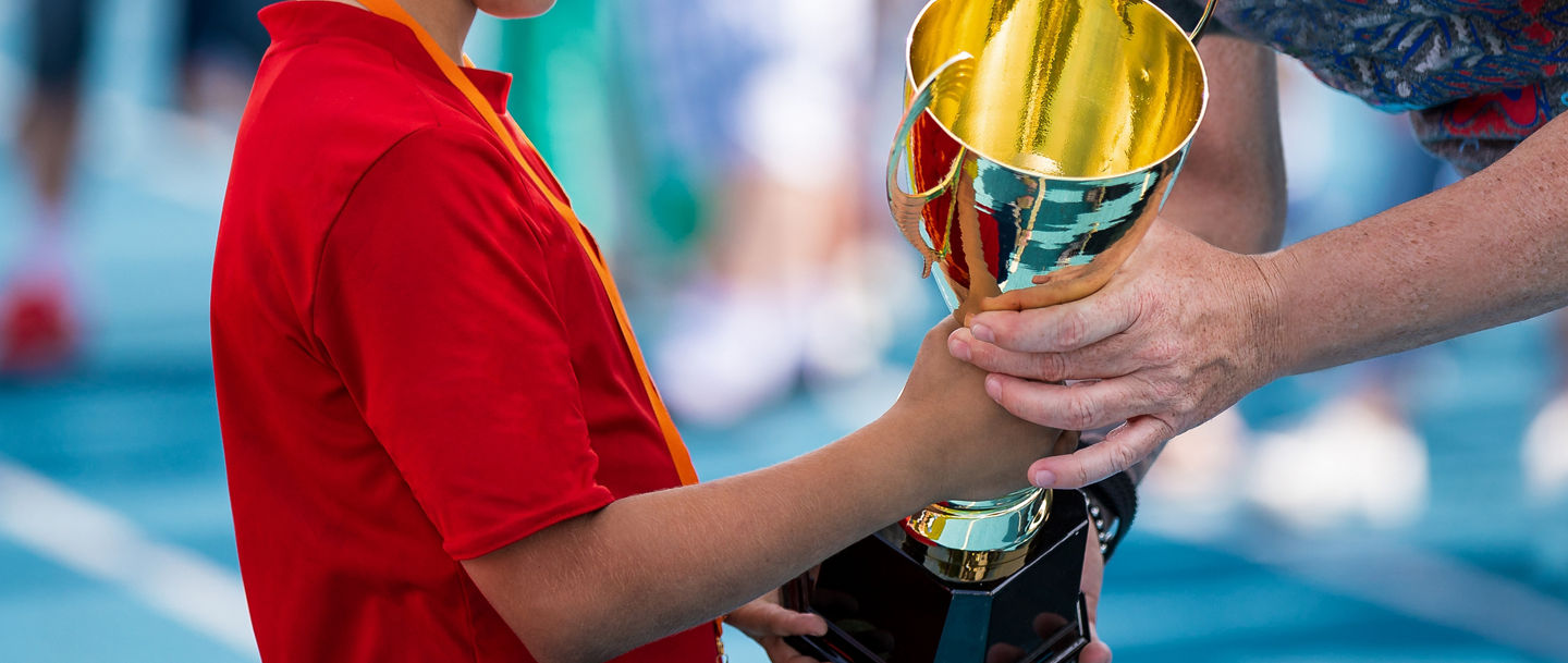 Child in a sportswear receiving a golden cup. Young athlete winning the sports school competition. Boy with golden medal getting an award for the best player of the tournament