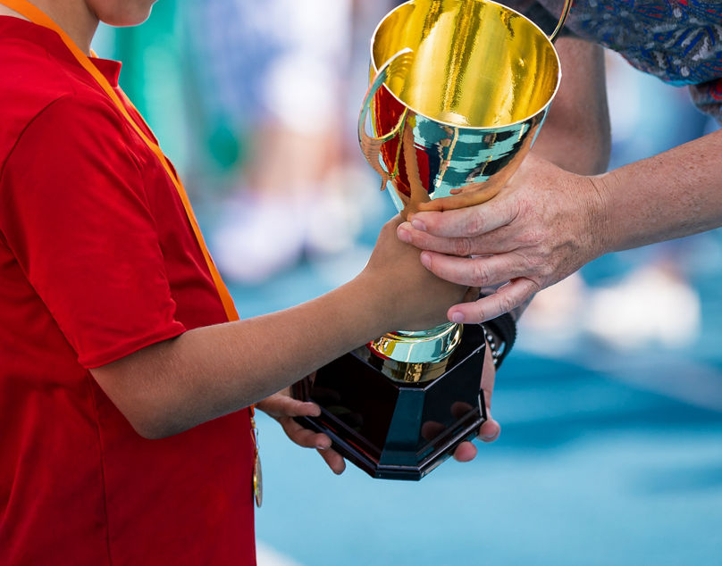 Child in a sportswear receiving a golden cup. Young athlete winning the sports school competition. Boy with golden medal getting an award for the best player of the tournament
