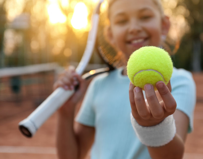 Cute little girl with tennis racket outdoors, focus on ball