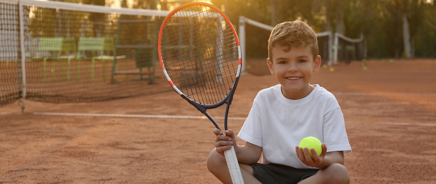 Cute little boy with tennis racket and ball on court outdoors