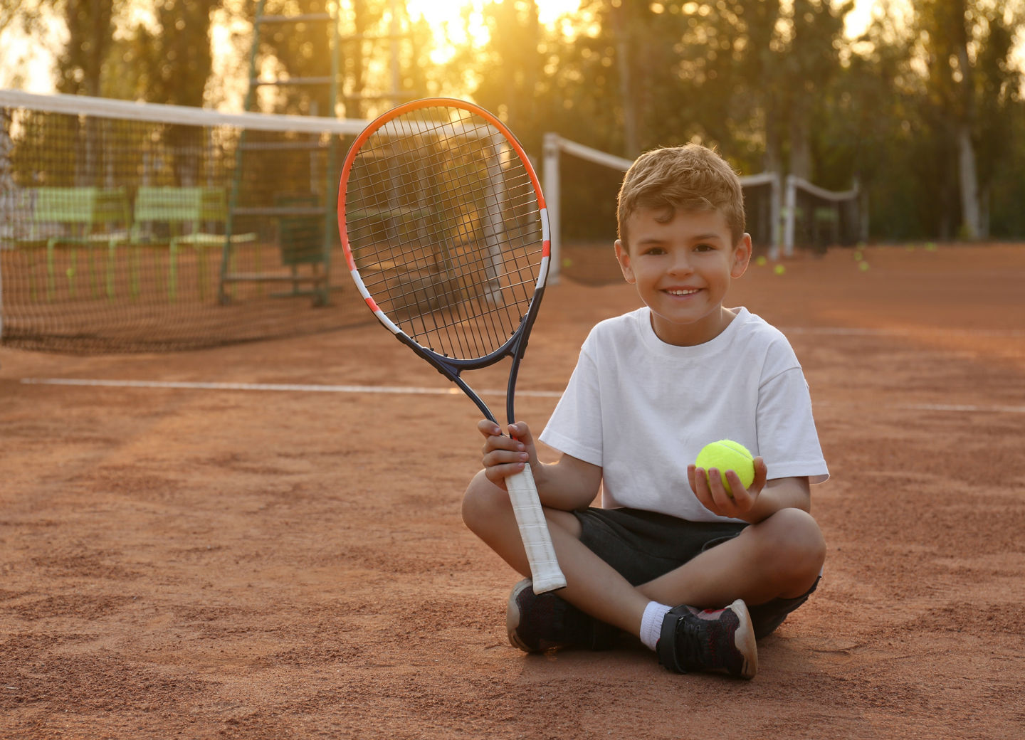 Cute little boy with tennis racket and ball on court outdoors