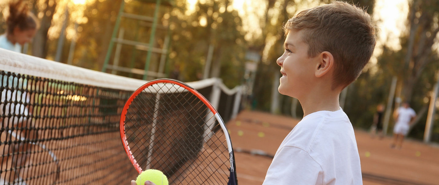 Cute little boy playing tennis on court outdoors