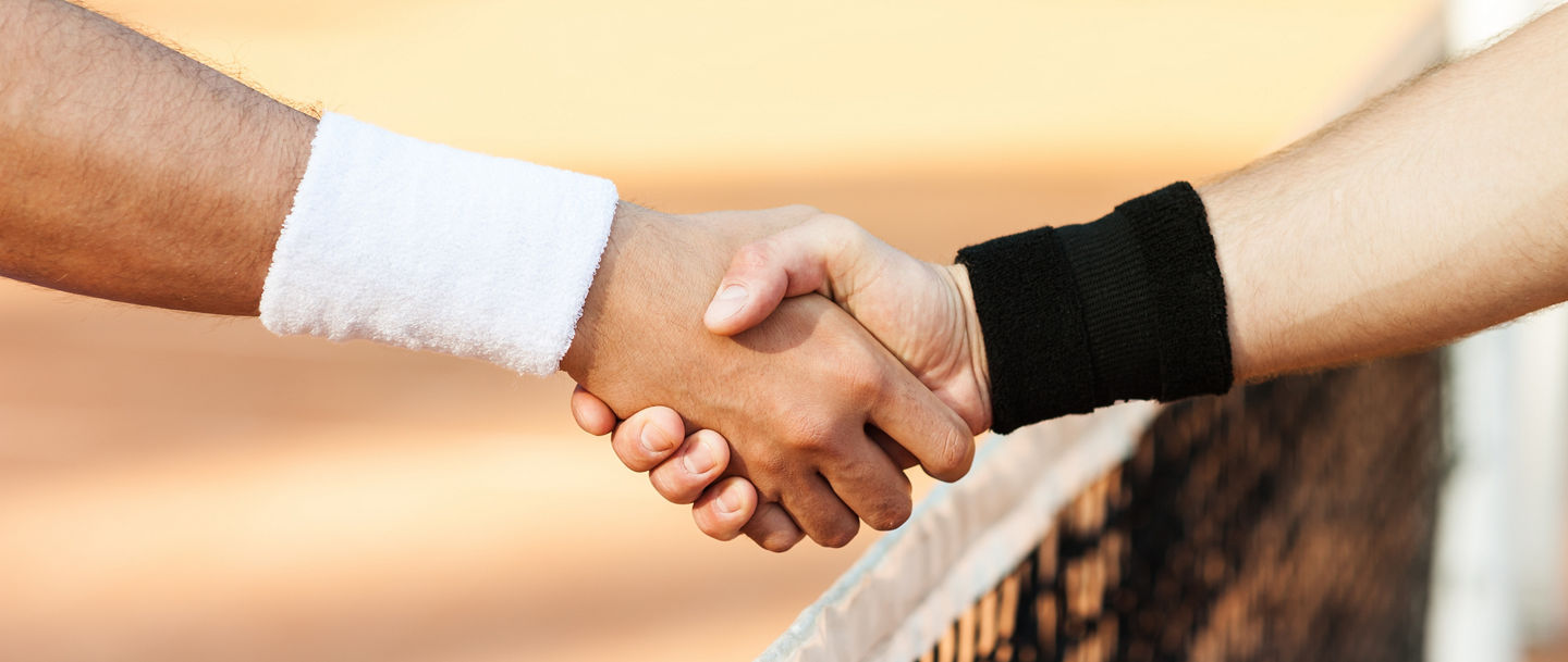 Close up photo of young men on tennis court. Men playing tennis. Men shaking hands above net before game