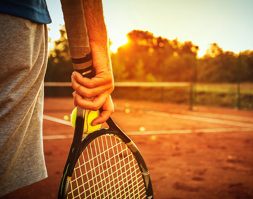 Mann steht mit Schläger und Ball in der Abendsonne auf dem Platz