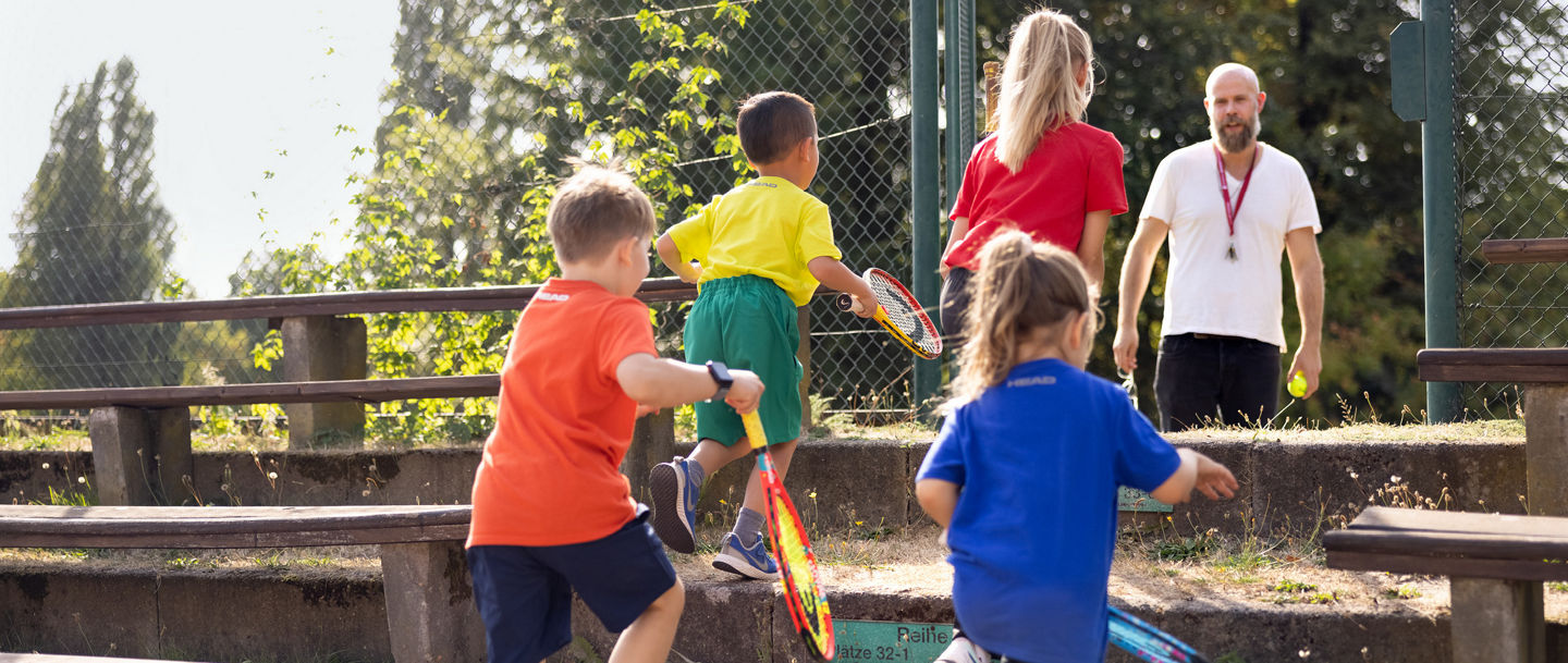 Eine Gruppe von Kindern läuft Stufen mit Tennisschlägern in der Hand hoch