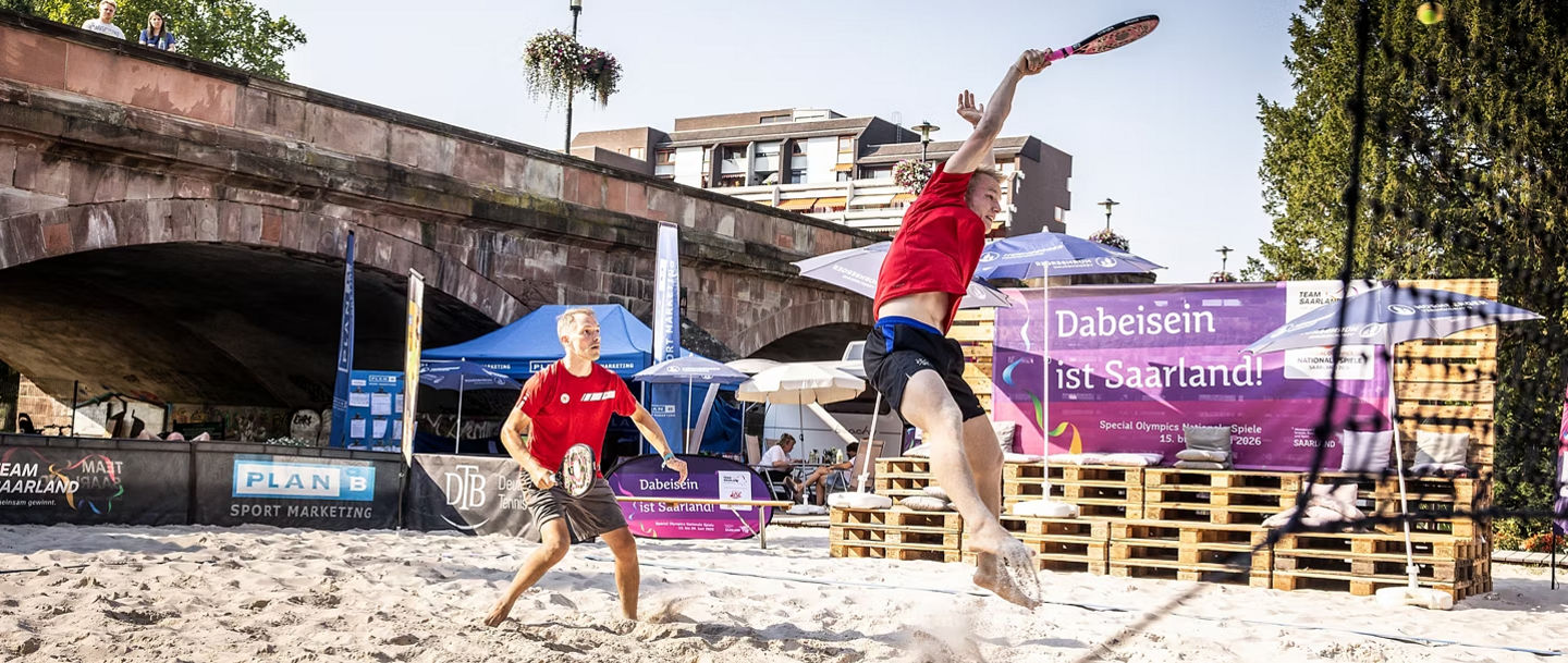 Herrenteam bei während dem Ballwechsel auf dem Beach Tennis Platz, einer springt gerade zum Ball
