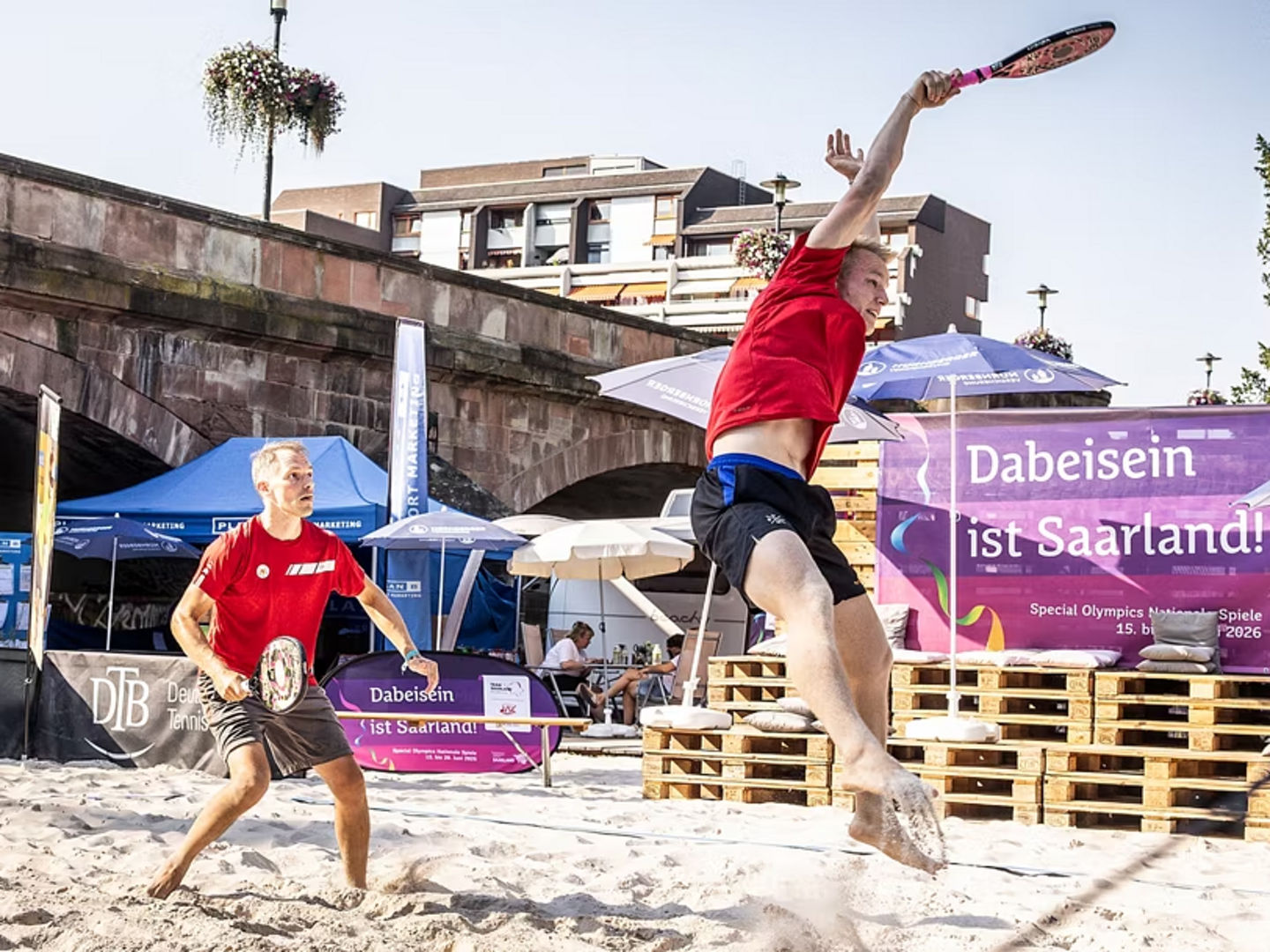 Herrenteam bei während dem Ballwechsel auf dem Beach Tennis Platz, einer springt gerade zum Ball