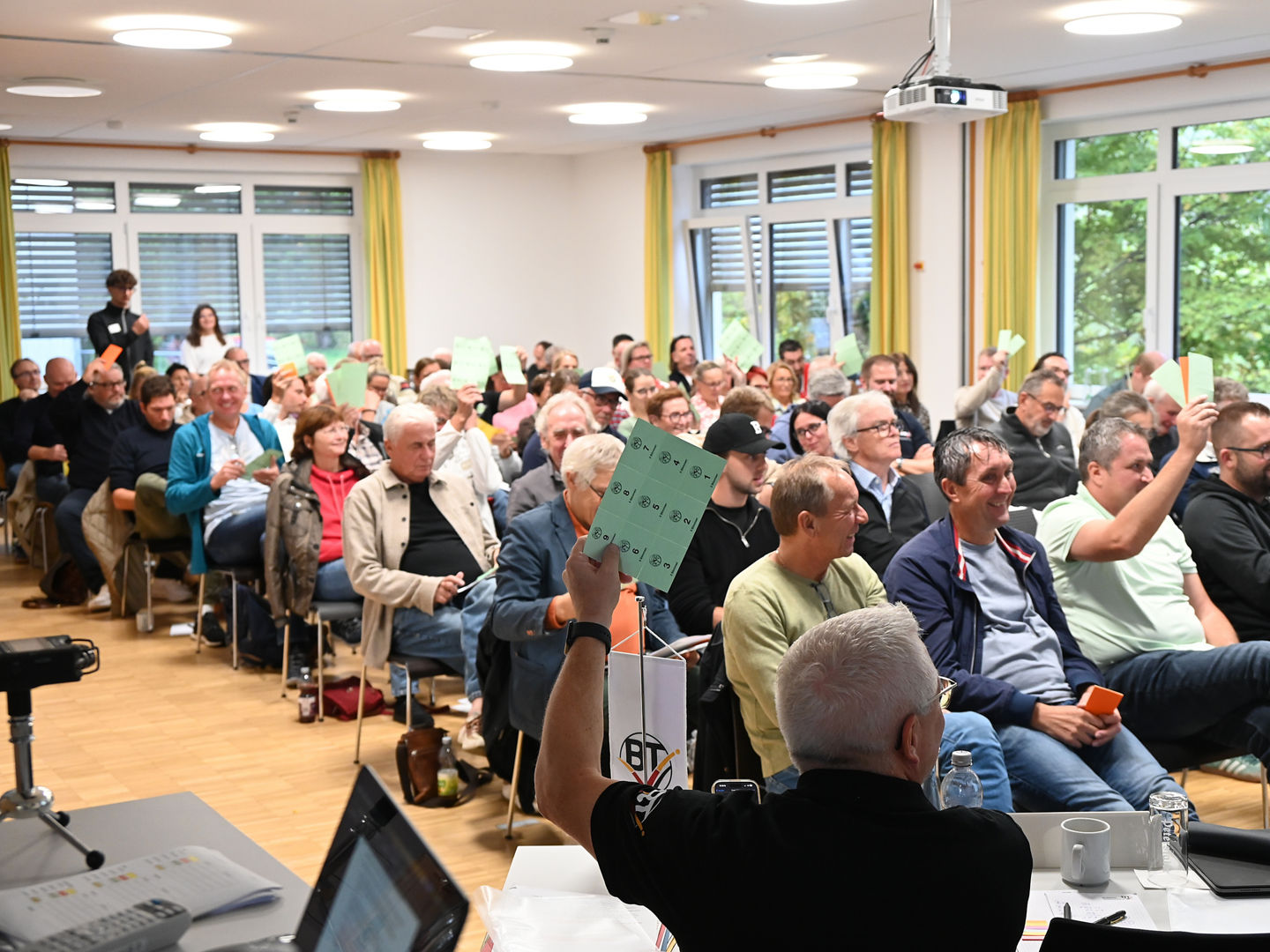 Voller Veranstaltungsraum mit sitzenden Menschen, die teilweise Stimmkarten in die Höhe halten