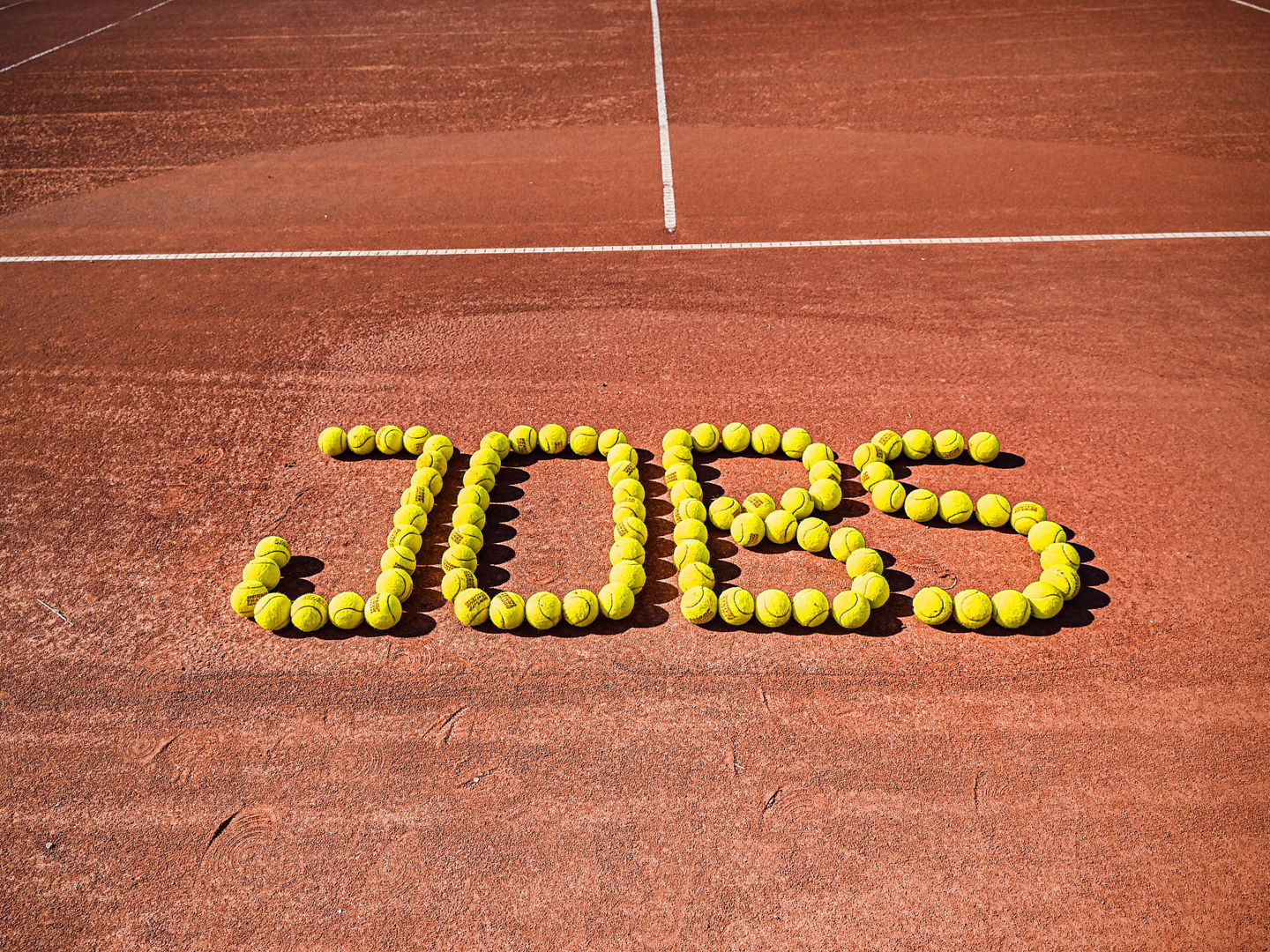 "Jobs"-Schriftzug mit Tennisbällen auf Tennisplatz