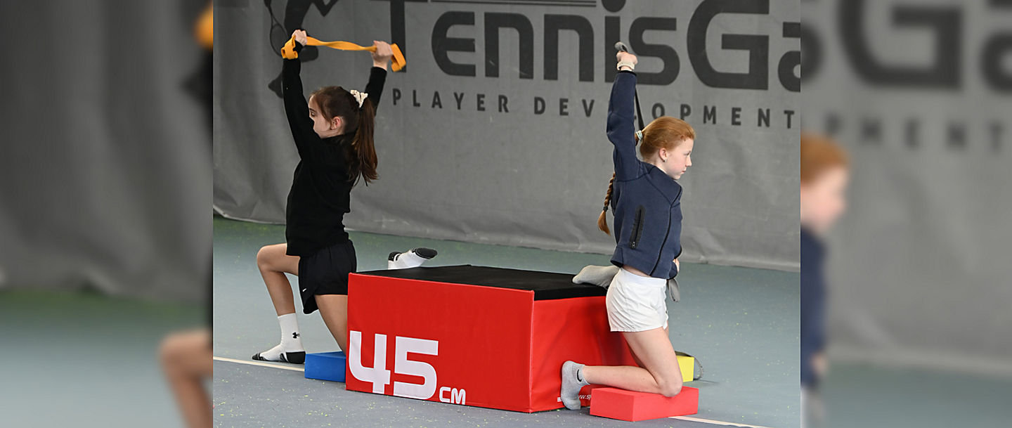 Zwei Tennisspielerinnen beim Mobilitätstraining auf dem Platz