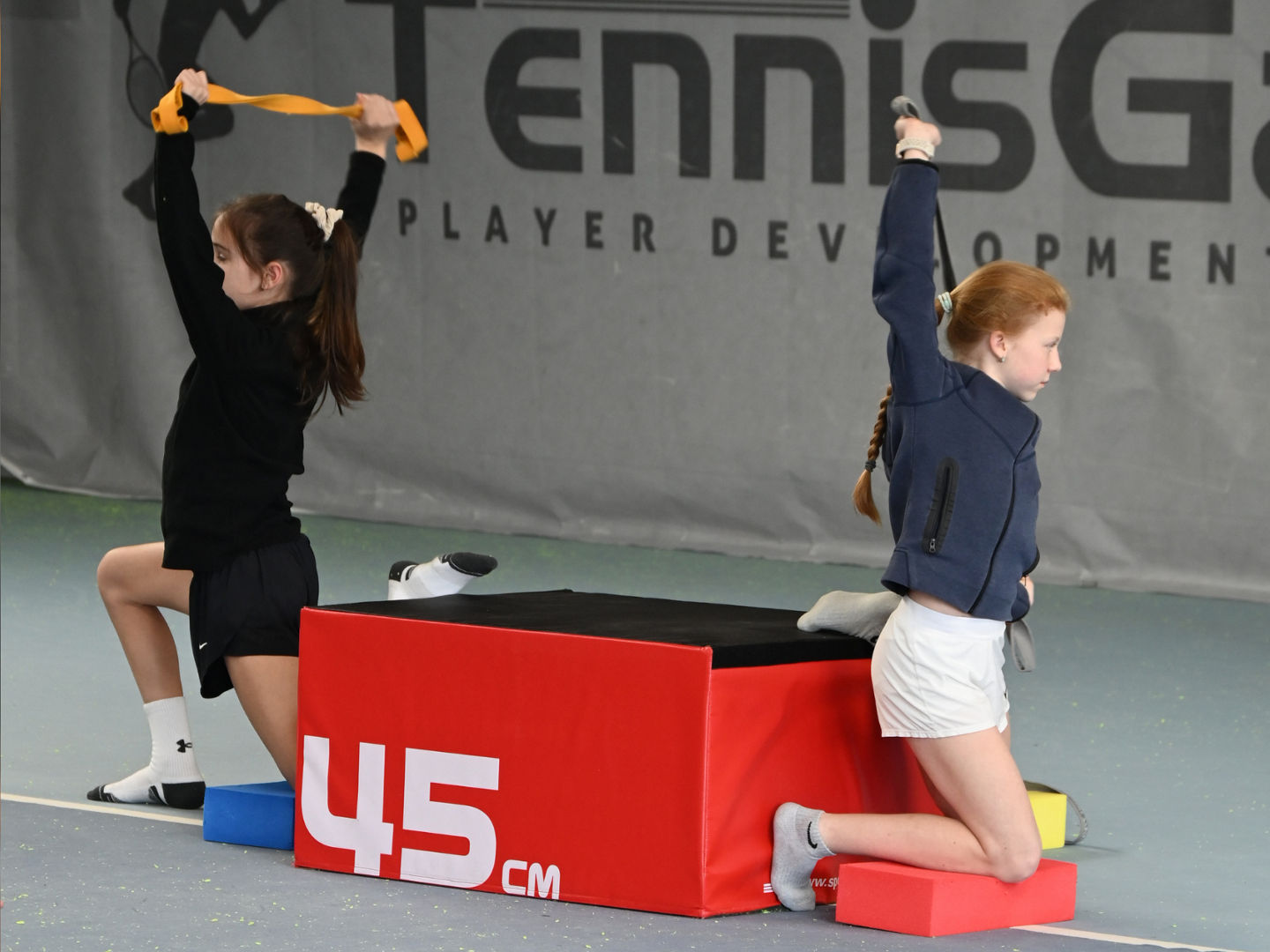 Zwei Tennisspielerinnen beim Mobilitätstraining auf dem Platz
