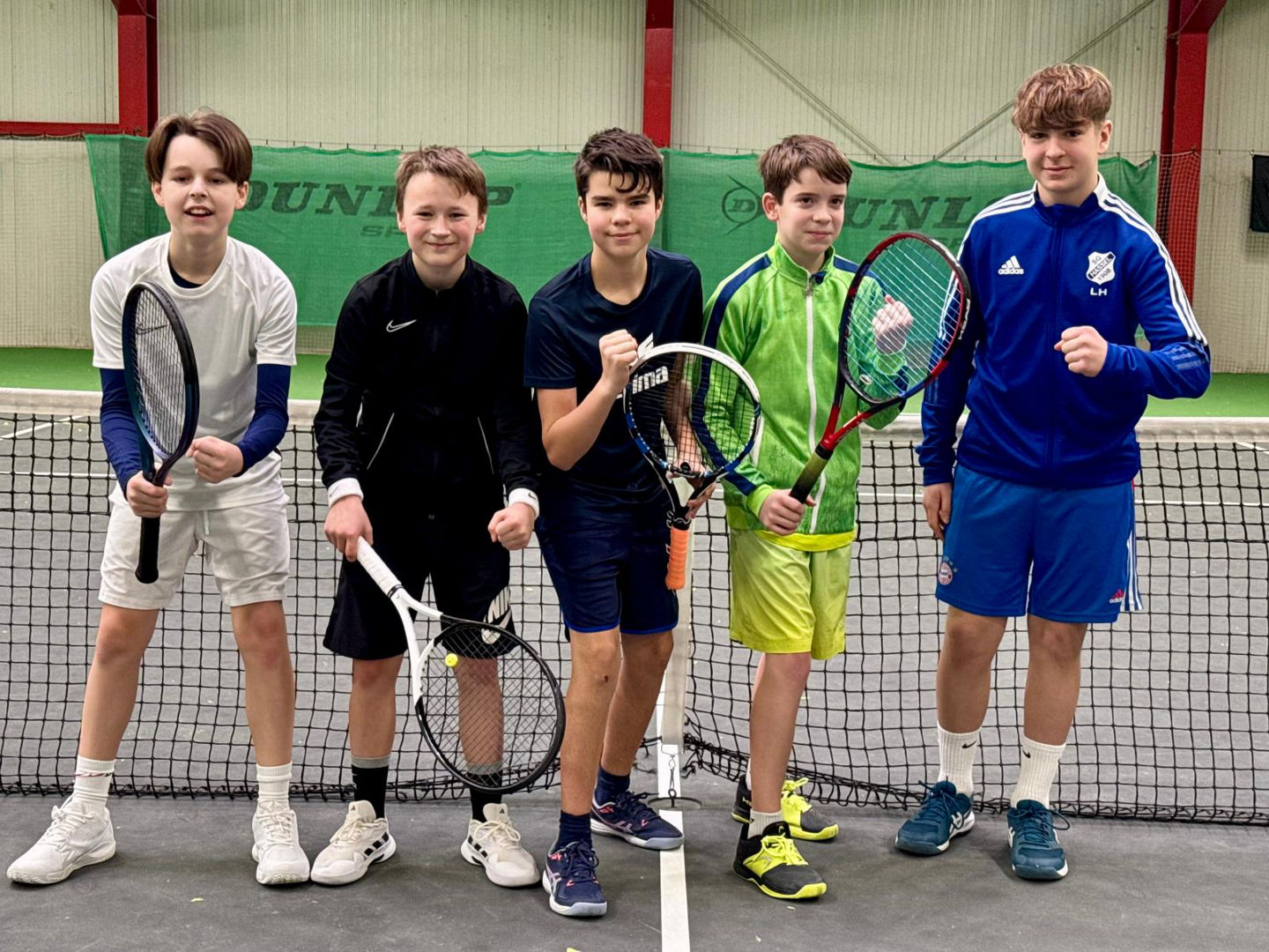 5 Jugendspieler in Jubelpose vor dem Tennisnetz in der Halle