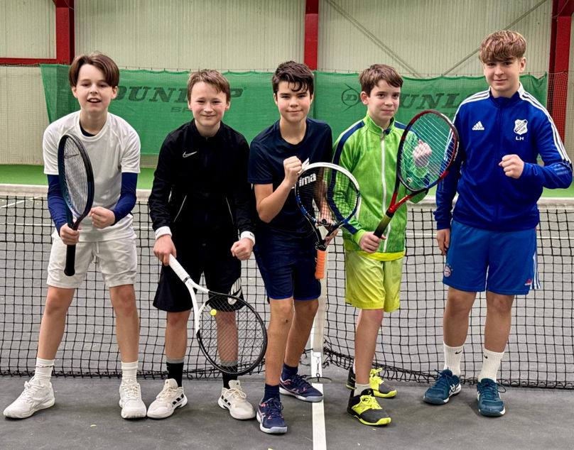 5 Jugendspieler in Jubelpose vor dem Tennisnetz in der Halle