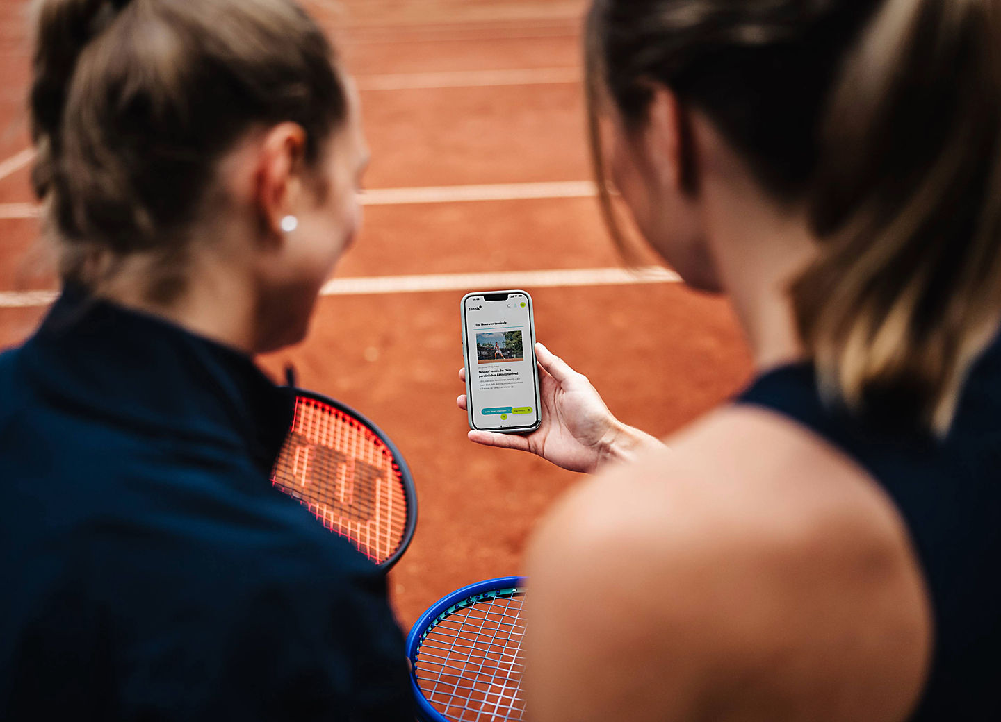 Zwei Tennisspielerinnen betrachten eine Smartphone