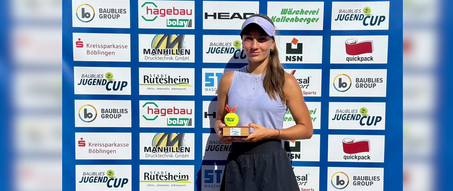 Julia Stusek mit dem Pokal in der Hand vor der Sponsorenwand des ITF-Turniers in Rutesheim