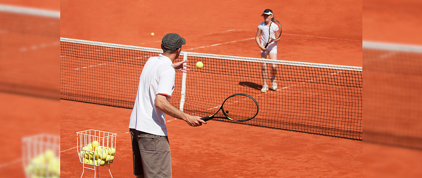 Tennistrainer mit Schülerin auf dem Sandplatz