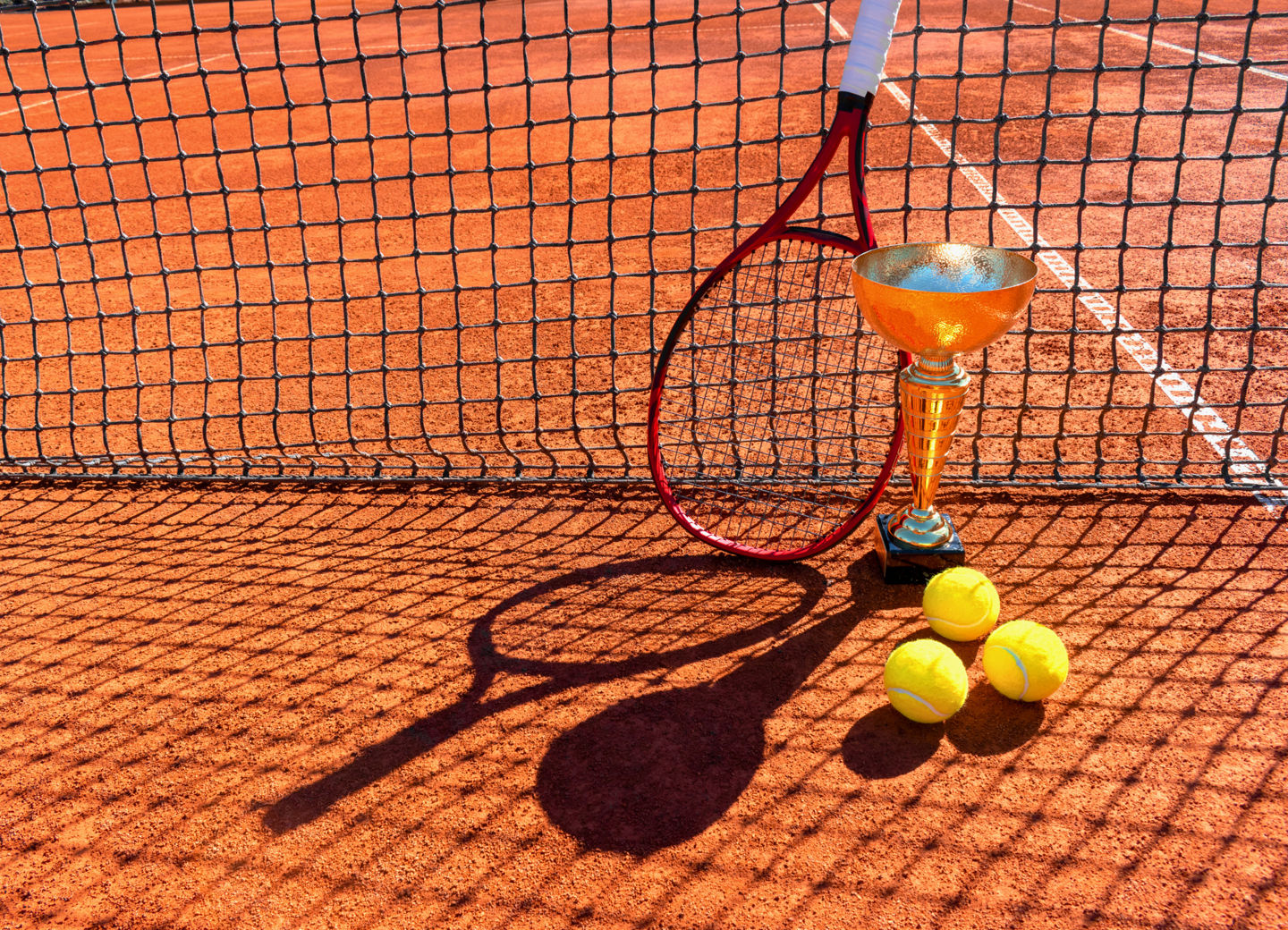 Tennischläger, -pokal und -bälle auf einem Tennisplatz vor einen Netz