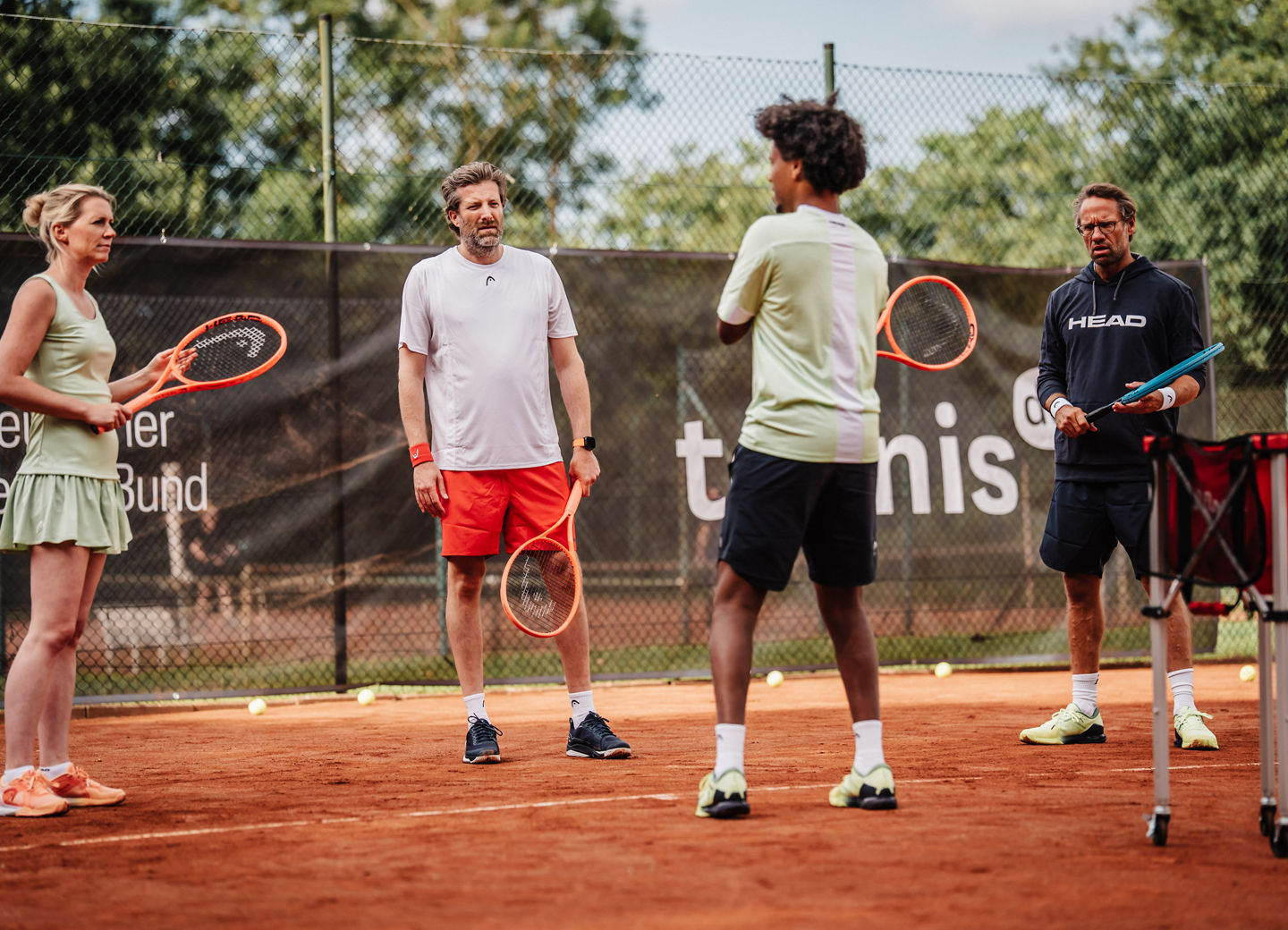 drei Tennisspieler:innen und ein Trainer auf dem Platz