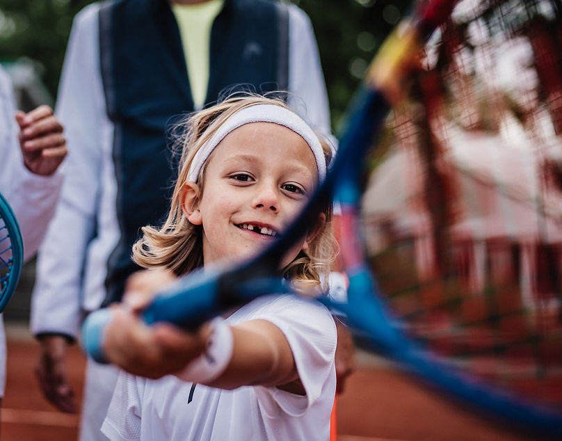 Kleiner Junge hält lächelnd seinen Schläger in die Kamera