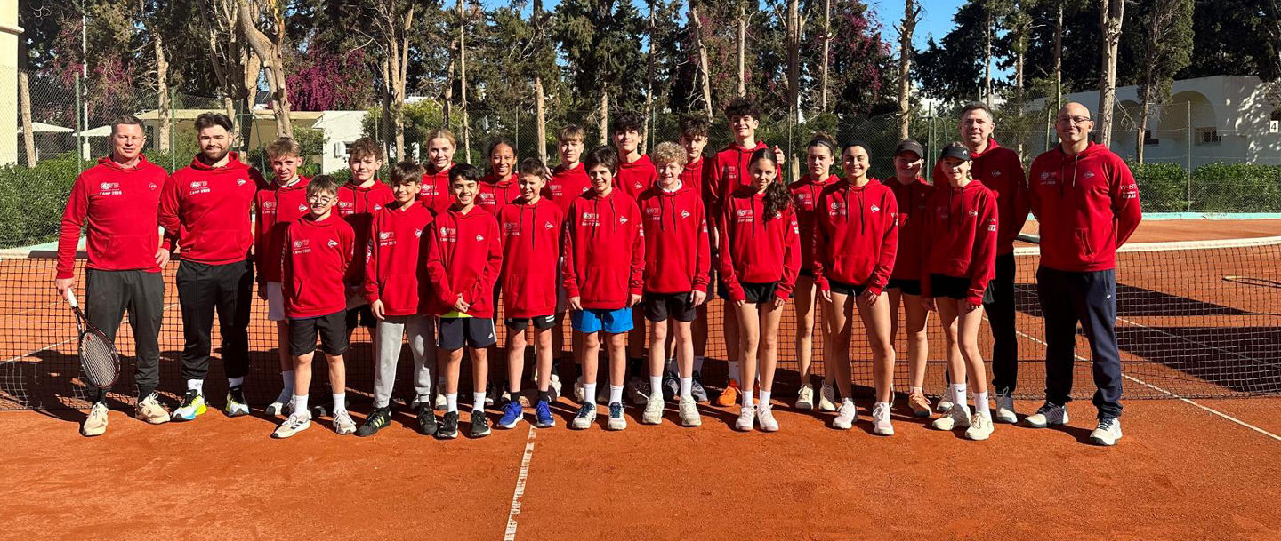 Kaderspieler:innen und Betreuer:innen auf dem Tennisplatz in Tunesien zum Gruppenfoto aufgestellt in roten, einheitlichen Pullis