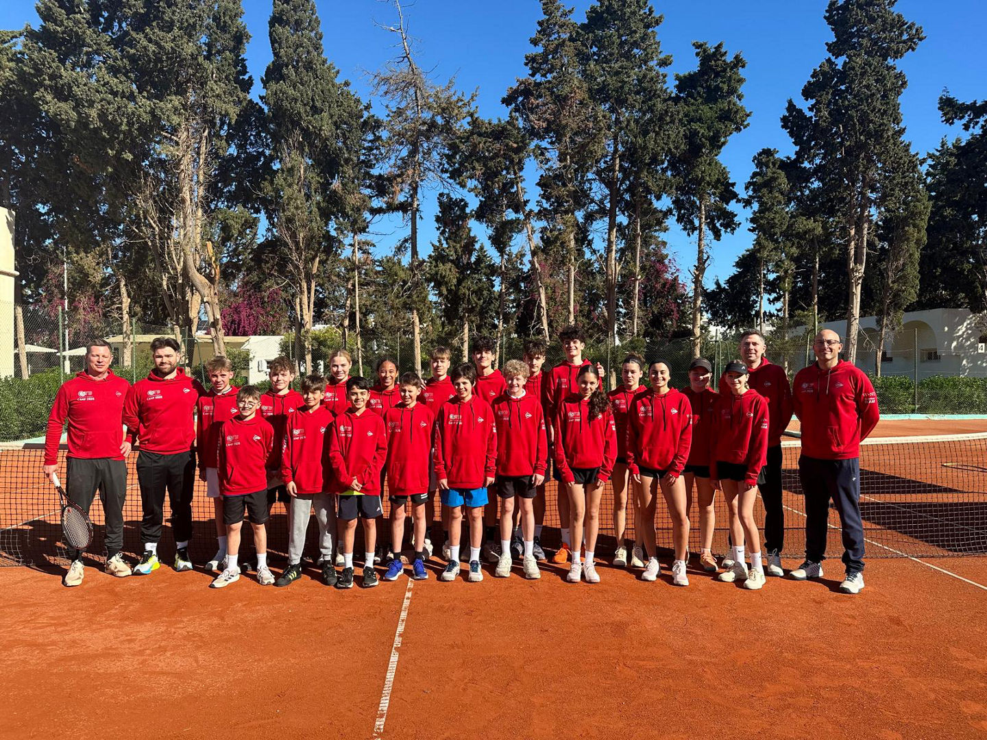 Kaderspieler:innen und Betreuer:innen auf dem Tennisplatz in Tunesien zum Gruppenfoto aufgestellt in roten, einheitlichen Pullis